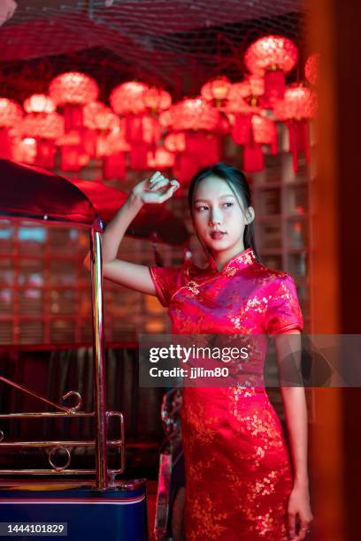 Studio portrait photo of a beautiful young asian female lady model wearing elegant red traditional chinese dress cheongsam costume with cool emotion look standing beside a tuk tuk taxi vehicle studio portrait photo beautiful young asian