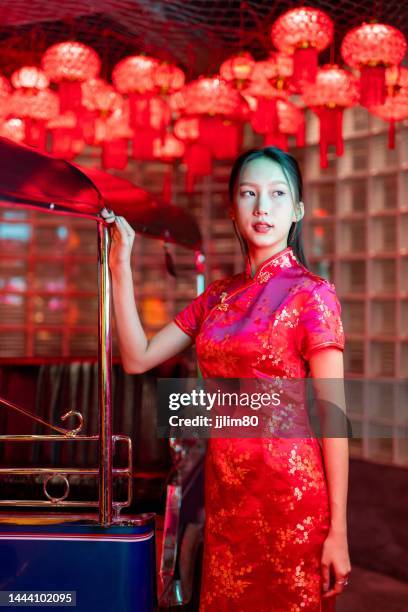 Studio portrait photo of a beautiful young asian female lady model wearing elegant red traditional chinese dress cheongsam costume with cool emotion look standing beside a tuk tuk taxi vehicle studio portrait photo beautiful young asian