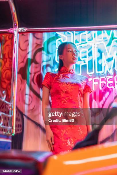 Studio portrait photo of a beautiful young asian female lady model wearing elegant red traditional chinese dress cheongsam costume with cool emotion look standing beside a tuk tuk taxi vehicle studio portrait photo beautiful young asian