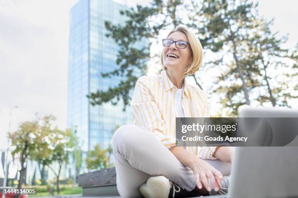 glückliche, reife geschäftsfrau, die einen laptop benutzt, wenn sie sich auf einer parkbank ausruht - einzelne frau über 40 stock-fotos und bilder