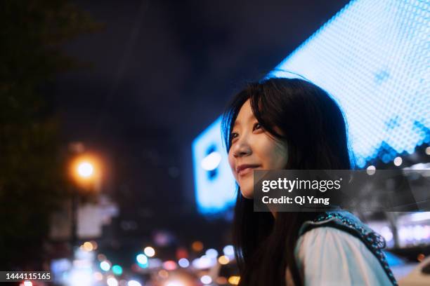 asian business woman using smartphone while standing in front of display screen on the street - ville intelligente photos et images de collection