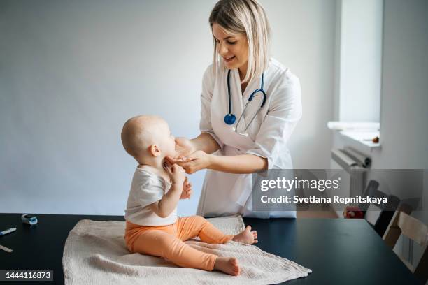 woman doctor pediatrician with a smile examines the baby in the clinic - european doctor stock-fotos und bilder