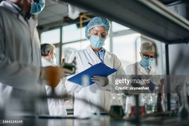 científica negra tomando notas mientras trabaja con sus colegas en el laboratorio. - calidad fotografías e imágenes de stock