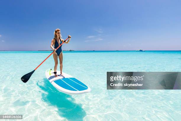 young woman enjoying in stand up paddle during summer day at sea. - maldives sport stock pictures, royalty-free photos & images