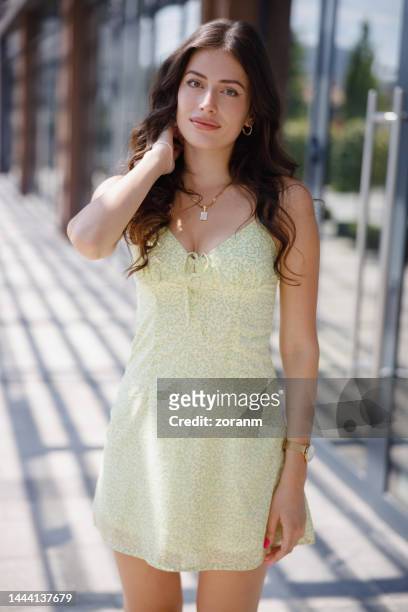 beautiful young woman in summer dress standing outdoors and looking at camera with hand in hair - mini dress stock pictures, royalty-free photos & images