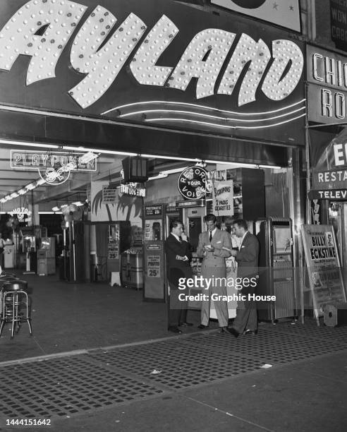 Man standing beneath the illuminated sign over the entrance to Playland on 42nd Street in New York City, New York, 1948. In the background are 'Take...