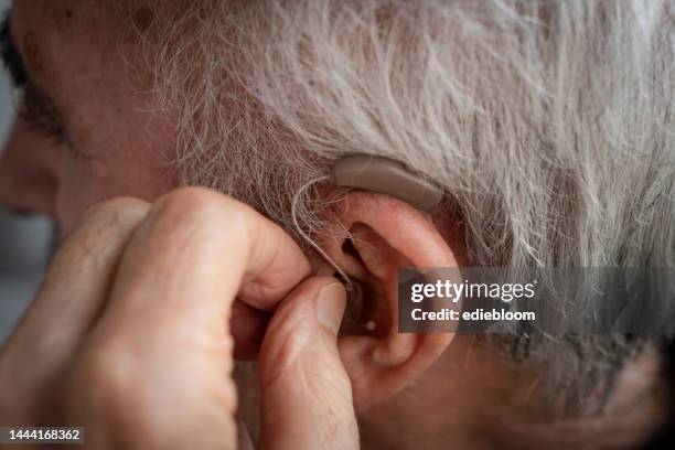 homem idoso que introduz seu aparelho auditivo - hearing aid - fotografias e filmes do acervo