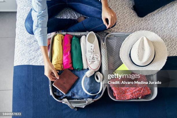 top view of an unrecognizable woman placing passport in an open suitcase with clothes and accessories for traveling. - passport open stock pictures, royalty-free photos & images