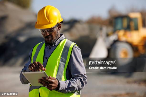 portrait of male engineer with hardhat using digital tablet while working at construction site - mijnindustrie stockfoto's en -beelden
