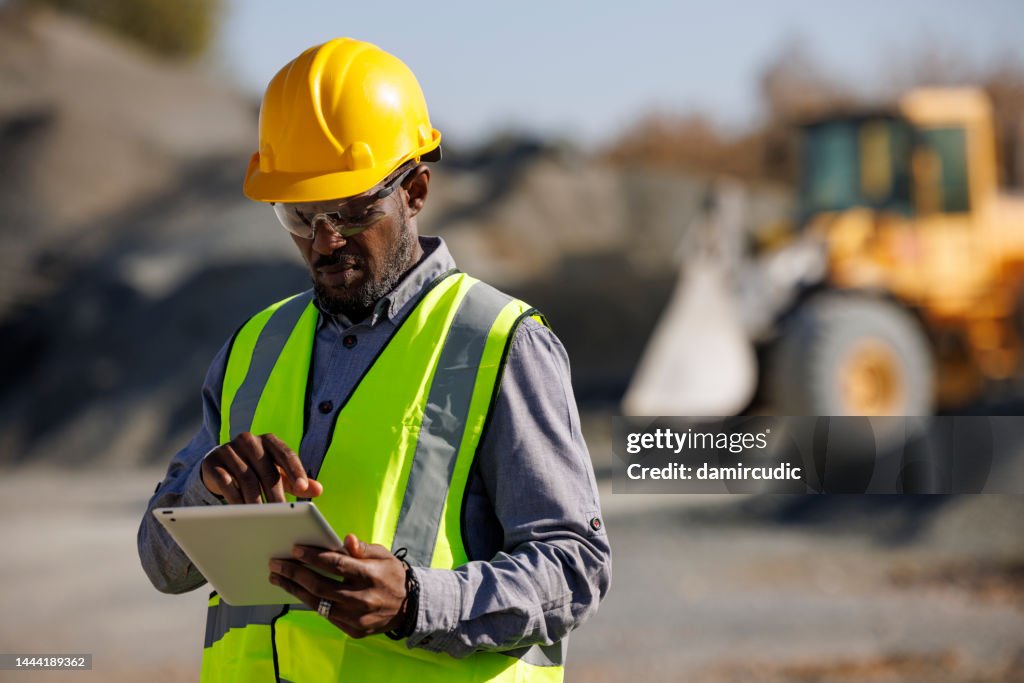 Portrait of male engineer with hardhat using digital tablet while working at construction site
