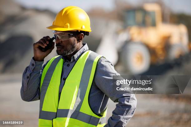 porträt eines industriearbeiters oder ingenieurs mit schutzhelm und schutzbrille mit walkie-talkie auf der baustelle - cb funk stock-fotos und bilder