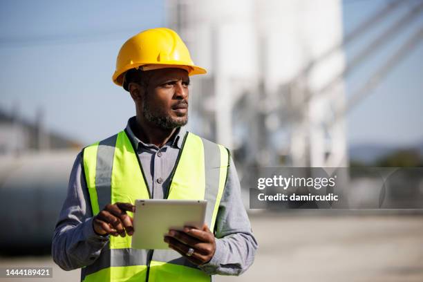 ritratto di ingegnere maschio con elmetto che utilizza tavoletta digitale mentre lavora sul suo cantiere - industria petrolifera foto e immagini stock