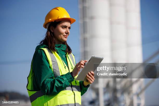 portrait of female engineer with hardhat using digital tablet while working on her work site - cement stock pictures, royalty-free photos & images