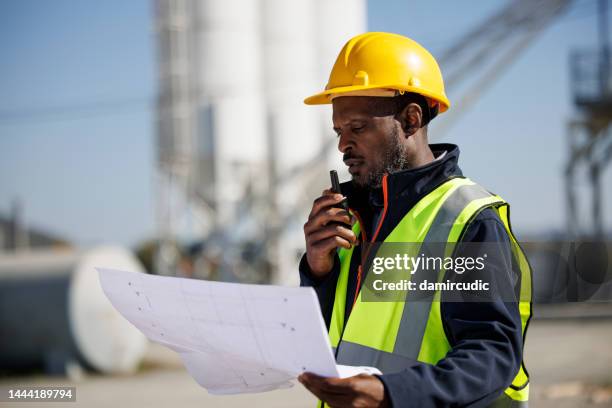 portrait of industry worker or engineer holding blueprint and using walkie-talkie at industrial facility - walkie talkie stock pictures, royalty-free photos & images