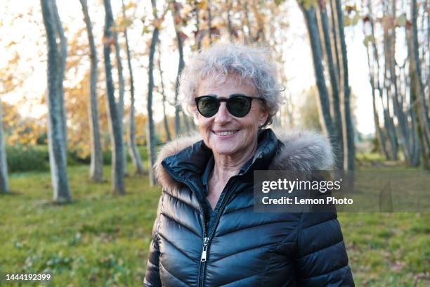 middle shot portrait of a beautiful confident senior woman looking at the camera and smiling in the forest - wavy hair stock pictures, royalty-free photos & images