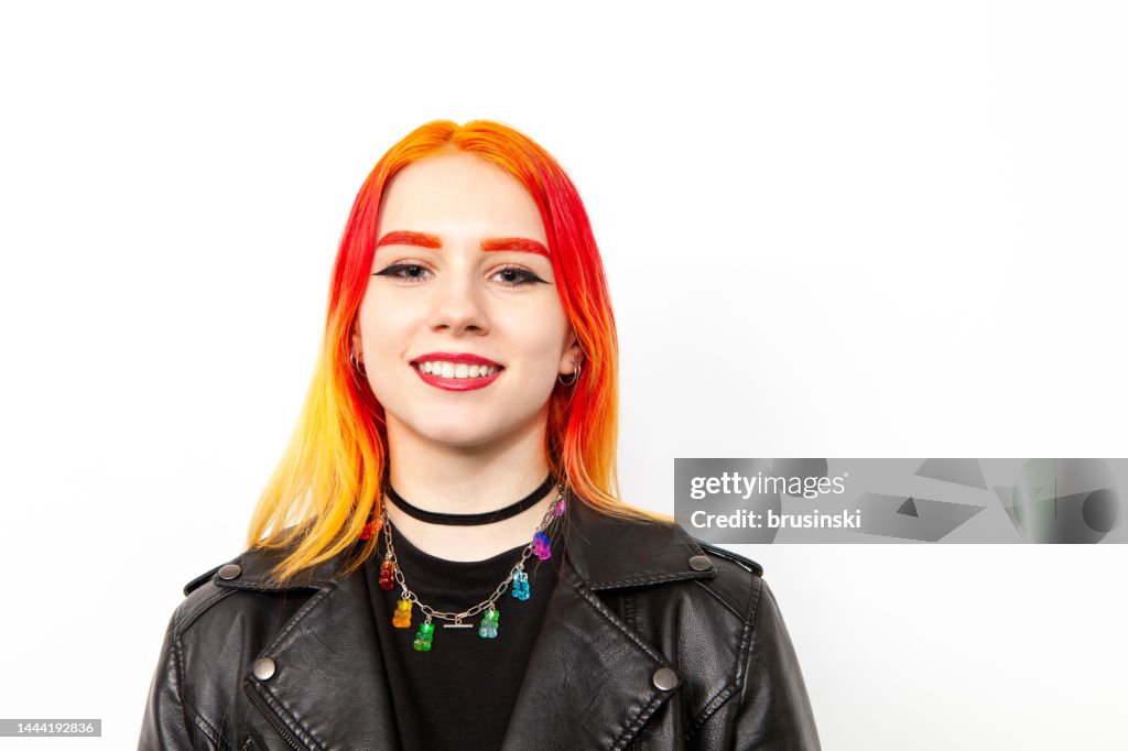 Close-up studio portrait of an 18 year old white woman with brightly dyed hair in a black leather jacket against a white background