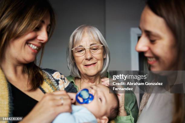 grandmother looking at her newborn grandson in the arm of his mother - gran stock pictures, royalty-free photos & images