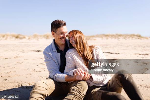 couple sitting on the beach looking at the sea enjoying a winter sunny day - 40s couple sunny stockfoto's en -beelden