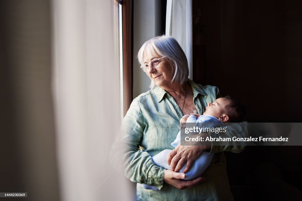 Aged woman holding her grandson while looking through the window