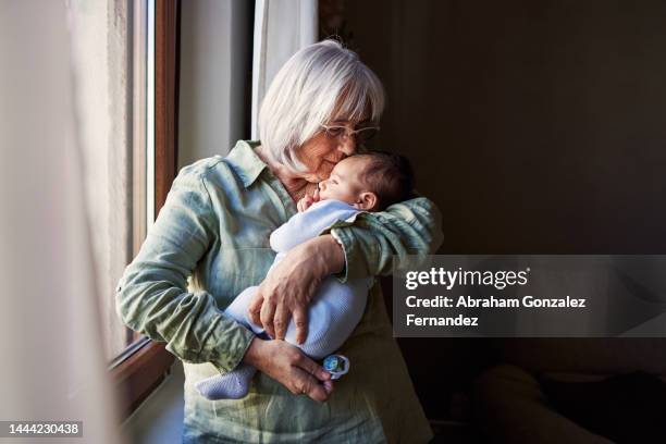 grandmother embracing tenderly a baby at home - mamie photos et images de collection