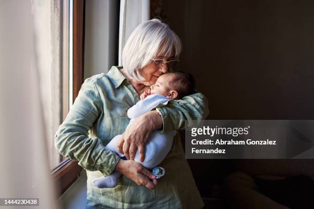 grandmother embracing tenderly a baby at home - grootmoeder stockfoto's en -beelden
