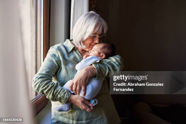 grandmother embracing tenderly a baby at home - grandma and baby stock pictures, royalty-free photos & images