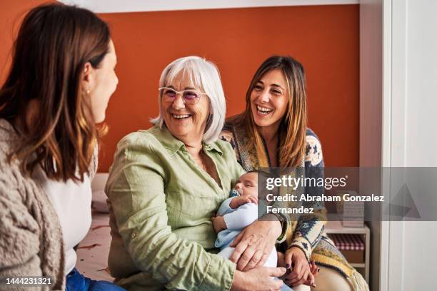 grandmother smiling while holding her grandson next to her daughters in a bedroom - familia multigeneracional fotografías e imágenes de stock