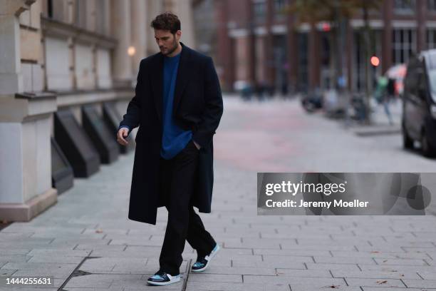 Felix Hartmann wearing a black Zara coat, blue Aylin Koenig sweater, black Aylin Koenig trousers, blue / white Air Jordan 1 Retro High OG UNC Patent...