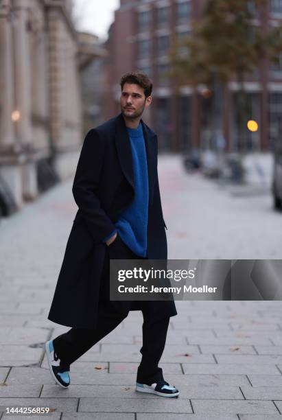 Felix Hartmann wearing a black Zara coat, blue Aylin Koenig sweater, black Aylin Koenig trousers, blue / white Air Jordan 1 Retro High OG UNC Patent...