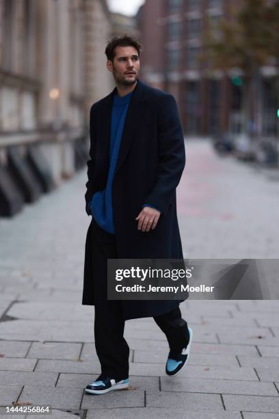 Felix Hartmann wearing a black Zara coat, blue Aylin Koenig sweater, black Aylin Koenig trousers, blue / white Air Jordan 1 Retro High OG UNC Patent...