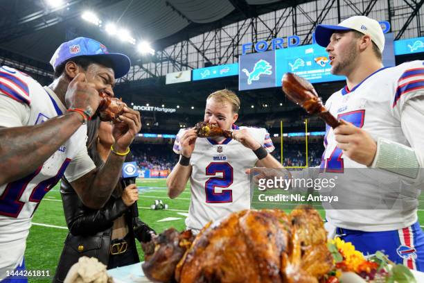 Stefon Diggs, Tyler Bass and Josh Allen of the Buffalo Bills celebrate on the field by eating turkey legs after defeating the Detroit Lions at Ford...