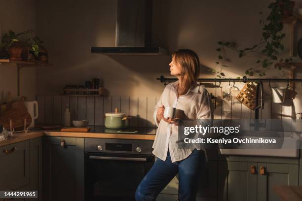 young woman using smartphone leaning at kitchen table with coffee mug and organizer in a modern home. smiling woman reading phone message. brunette happy girl typing a text message - coffee table reading mug stock pictures, royalty-free photos & images