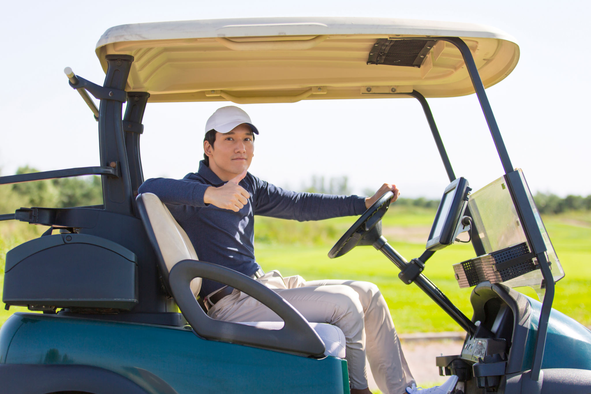 Young East Asian man driving an electric golf cart Young East Asian man driving an electric golf cart