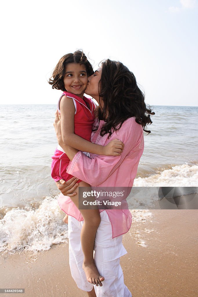 Mother holding and kissing her daughter on the Beach