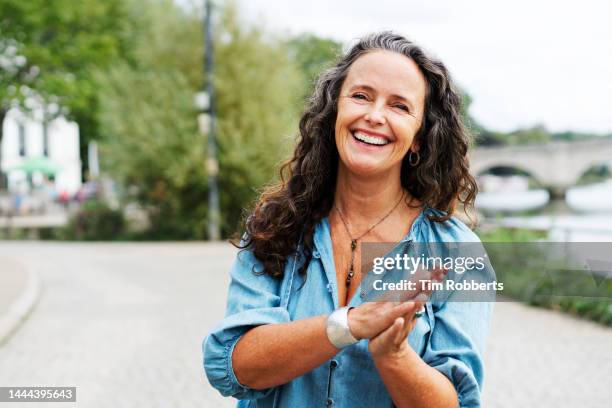 woman with hands together looking at camera, smiling - quinquagénaire photos et images de collection