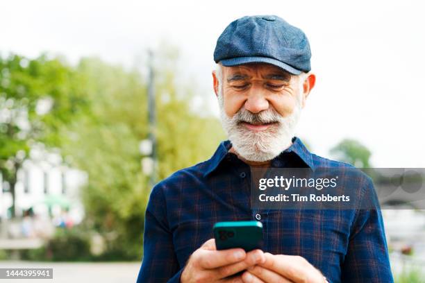 man using smart phone, wearing hat - senior men stock pictures, royalty-free photos & images