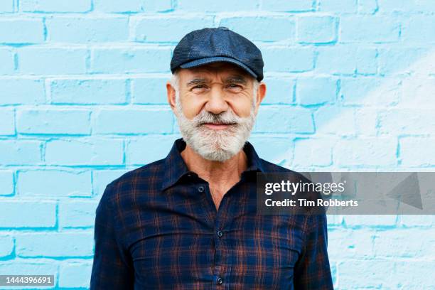 man looking at camera next to blue wall - old hipster stock-fotos und bilder