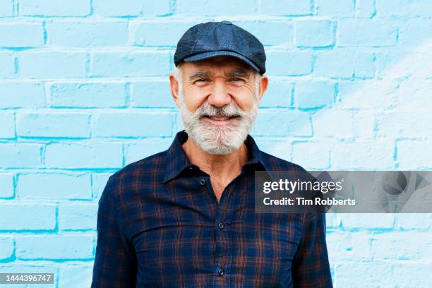 man looking at camera, smiling, blue wall - baby boomer stock pictures, royalty-free photos & images