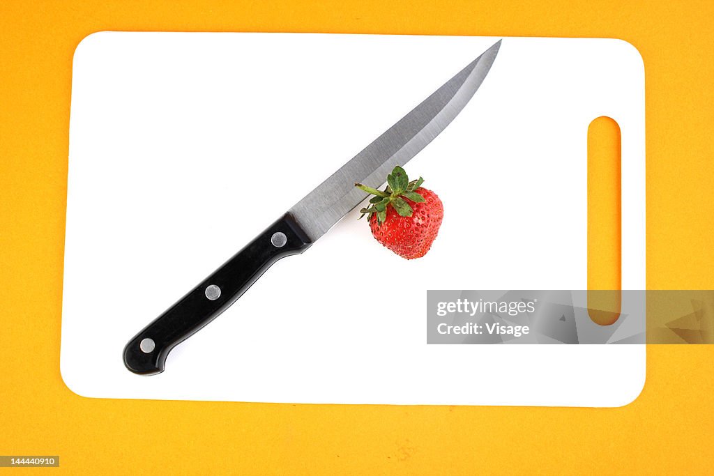 A strawberry on a cutting board with a knife