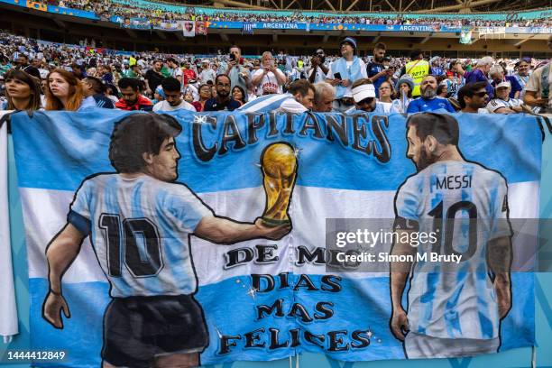 Detail of a Argentina flag featuring Diego Maradona handing the FIFA World Cup trophy to Lionel Messi alongside Argentina fans in the stands during...