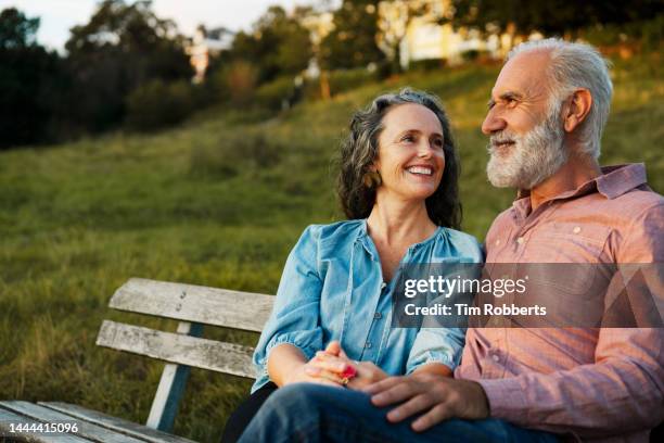 man and woman on bench, smiling - pensions stock-fotos und bilder