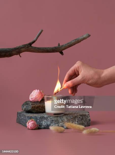 hand lighting vanilla candle standing on a stone. natural minimalistic still life composition with roses, branches and dry rabbit tail grass - match lighting equipment fotografías e imágenes de stock