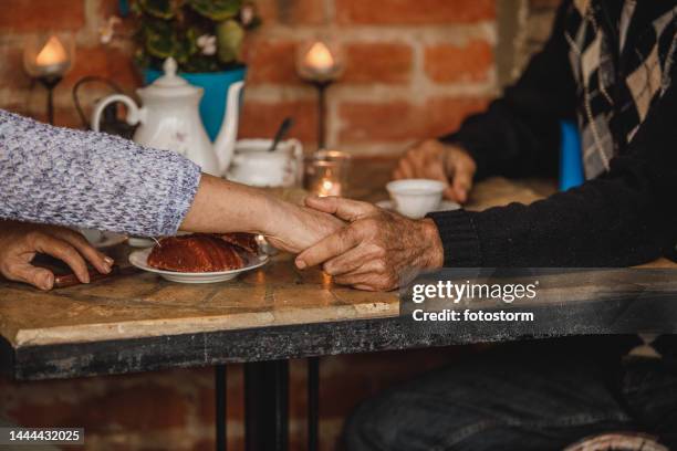 affectionate senior couple holding hands while enjoying afternoon tea in a romatic setting on their patio - old couple restaurant stock pictures, royalty-free photos & images