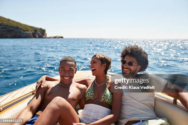 happy young friends sitting together in motorboat - season 3 stockfoto's en -beelden