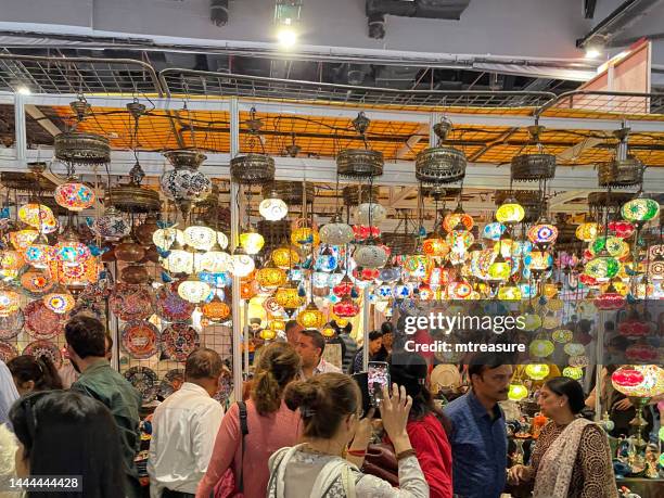 image of traders and customers at trade fair, many colourful, mosaic glass sphere lights hanging suspended from ceiling, illuminated glowing moroccan style lanterns interior lighting, focus on foreground - trade show stock pictures, royalty-free photos & images