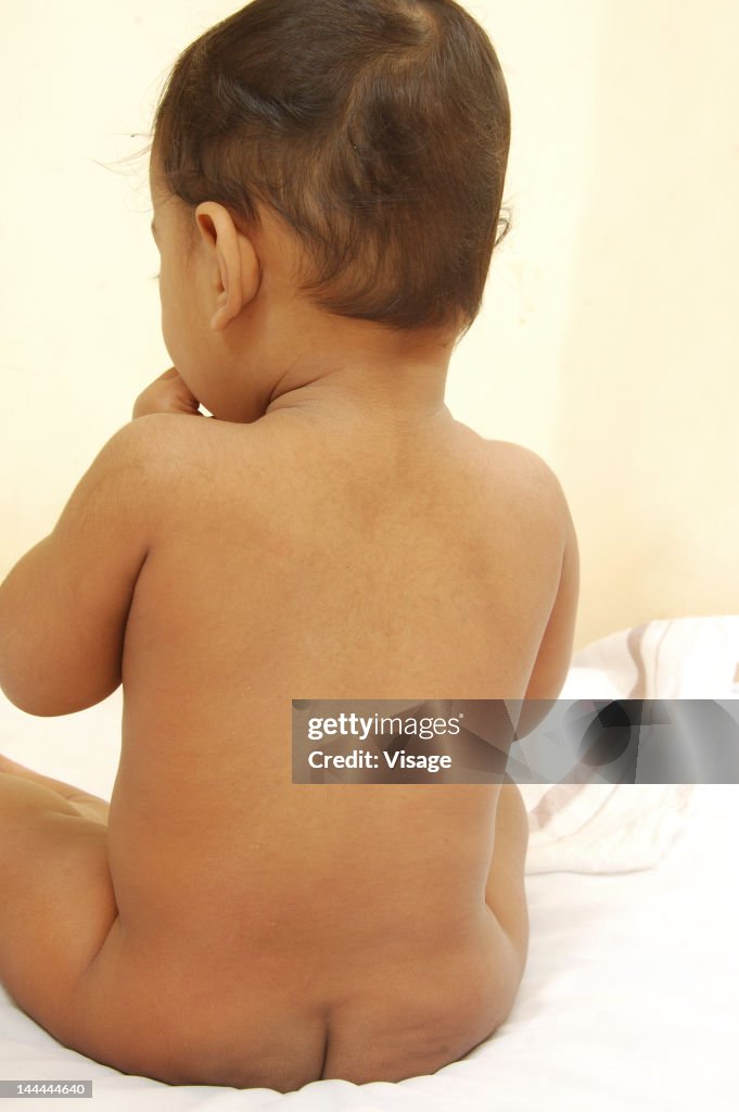 Rear view of a baby sitting on a bed