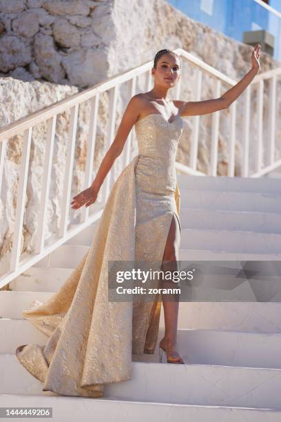 beautiful young woman in long champagne sleeveless dress standing on staircase and looking at camera - 長全身裙 個照片及圖片檔