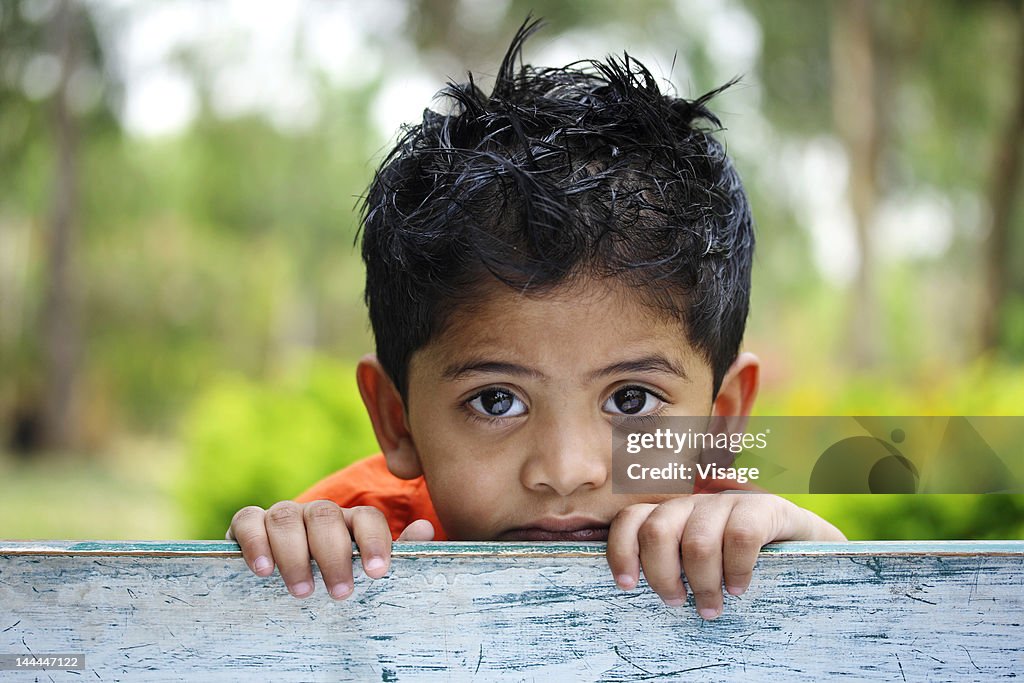 Close up of a young kid looking from behind a bench