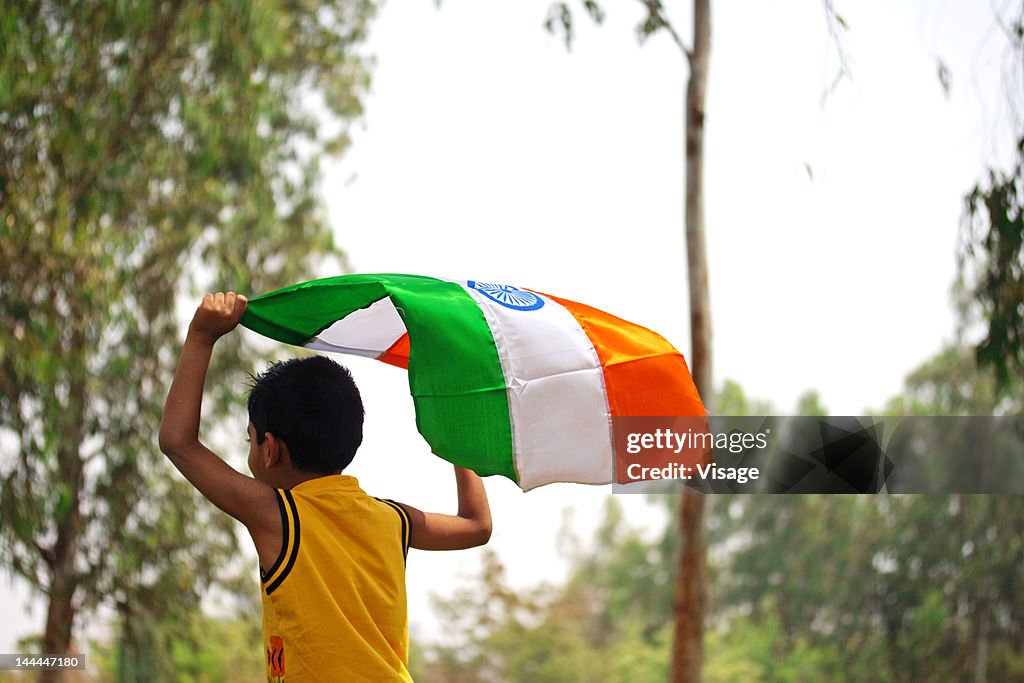 A kid running ,holding the tri-colour flag above his head