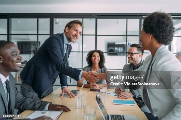 empresaria y hombre de negocios dándose la mano sobre la mesa. - fusiones y adquisiciones fotografías e imágenes de stock